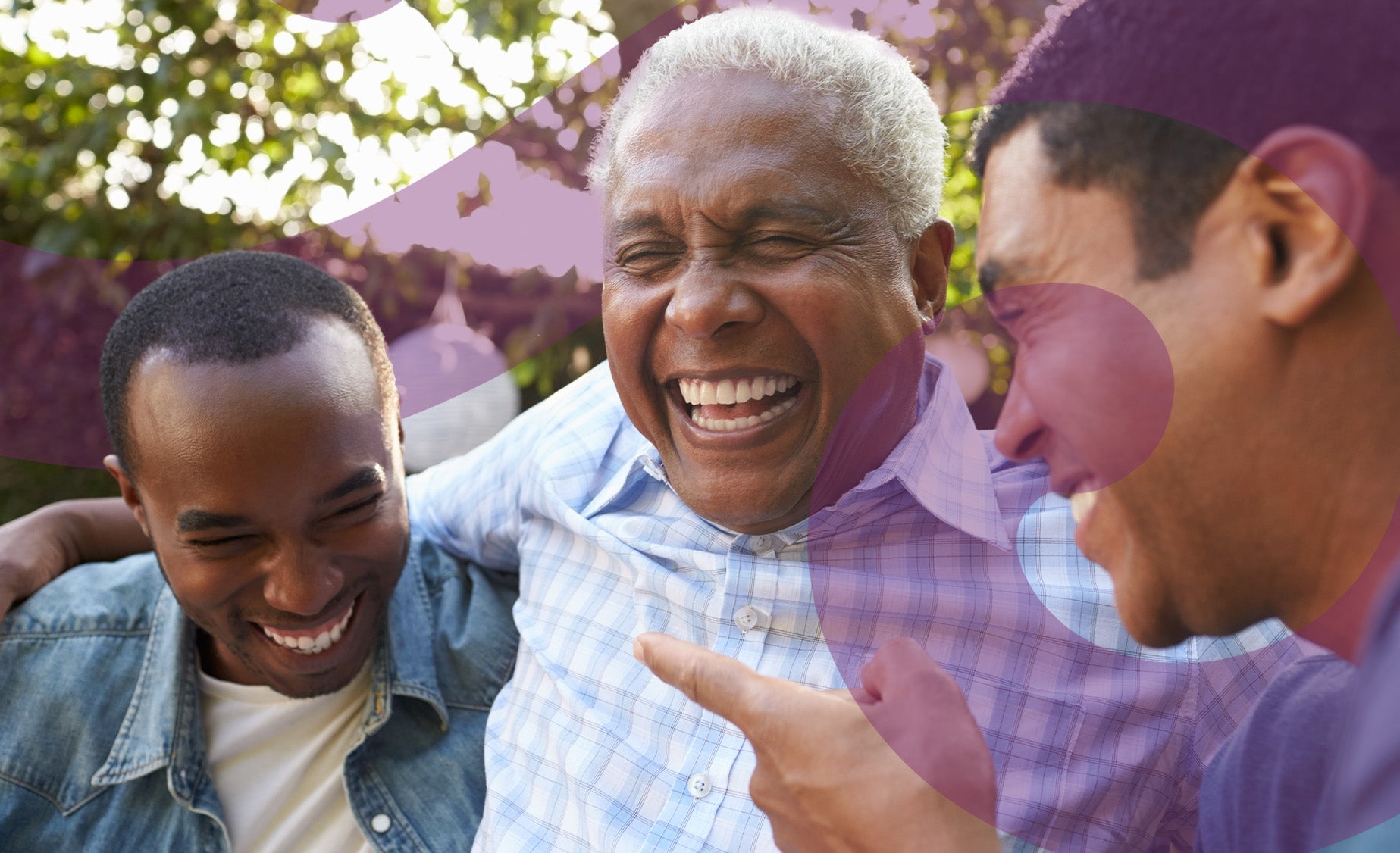 Two men laugh with their elderly father, arms round each other, and trees in the background 