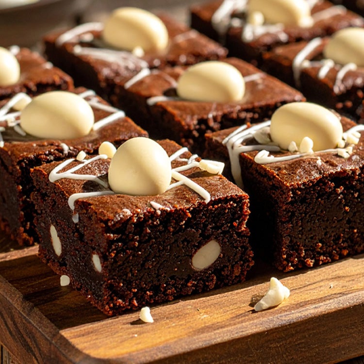 Chocolate brownies on a wooden board with Milkybar white chocolate mini eggs throughout and pressed into the top