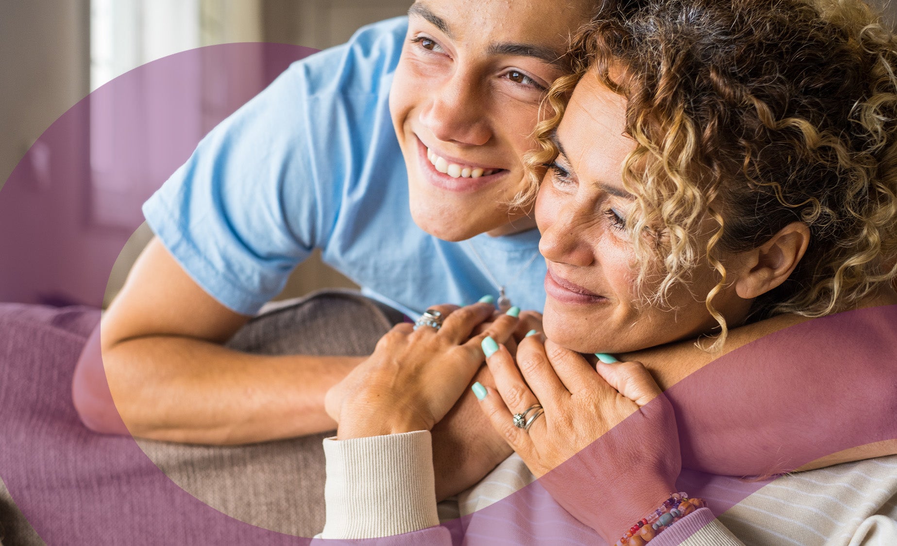 A young man hugging his mother on a cosy-looking sofa 