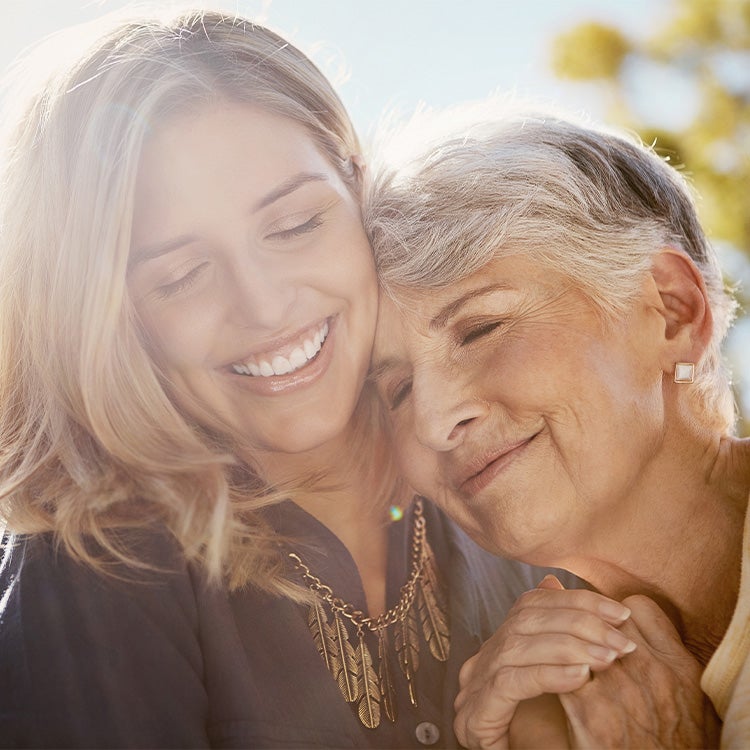  A woman hugging her mother with sunlight and trees in the background
