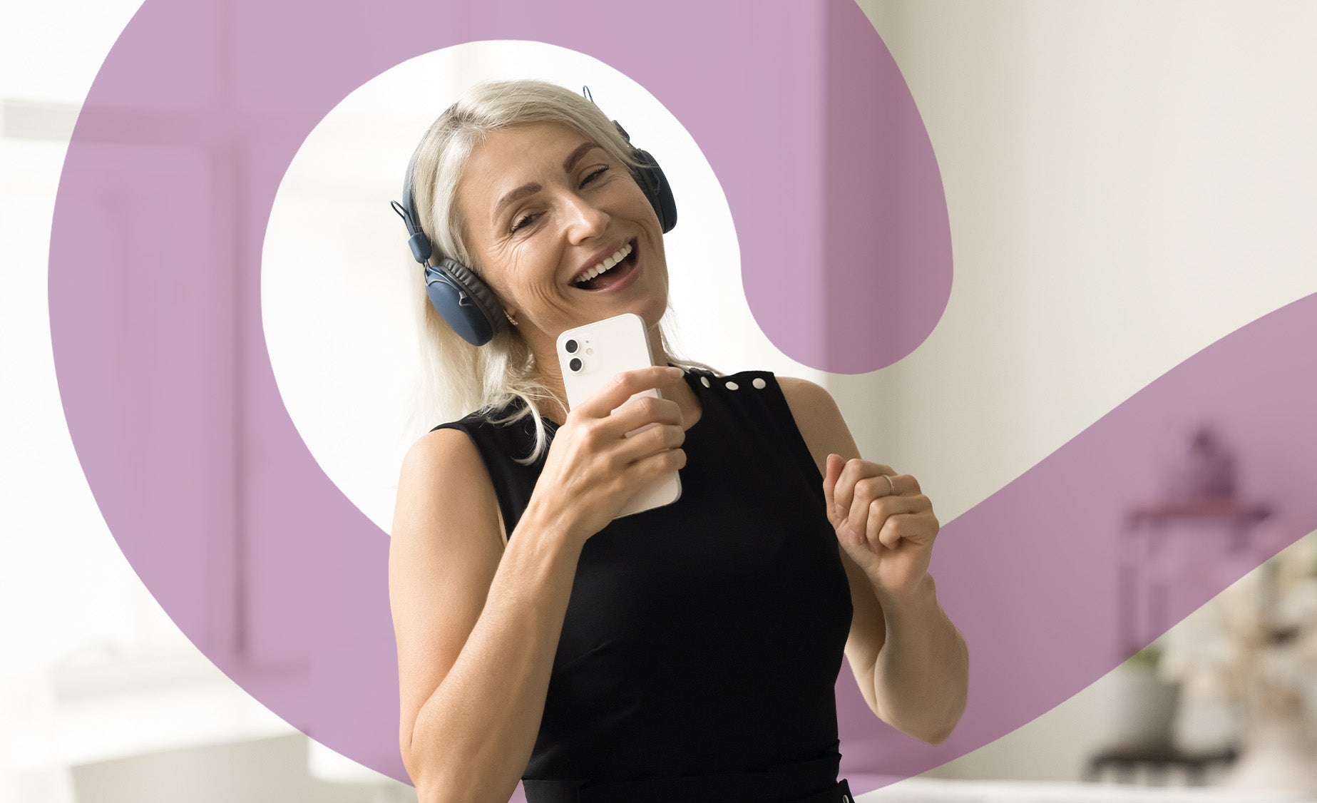 A woman wearing headphones dances in her living room holding her phone 