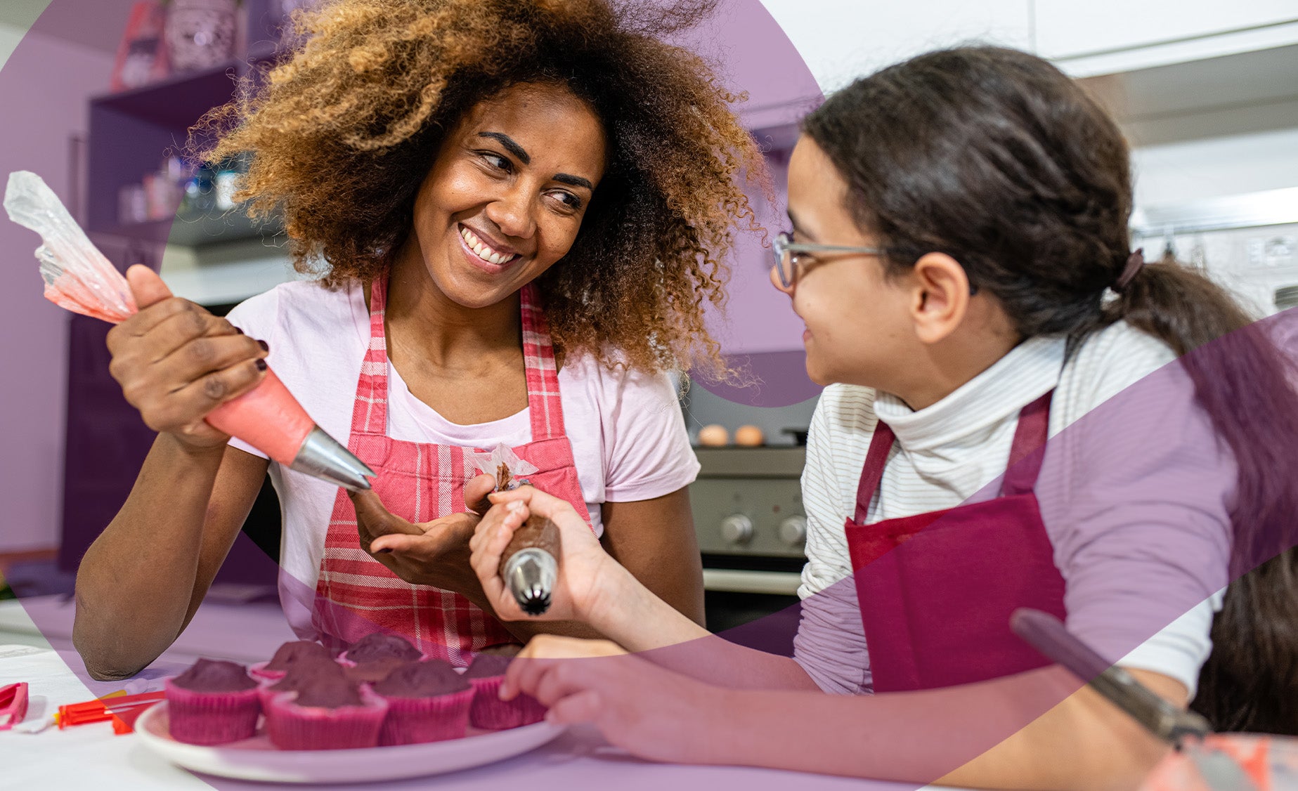 A girl decorates cupcakes with her mum in the kitchen
