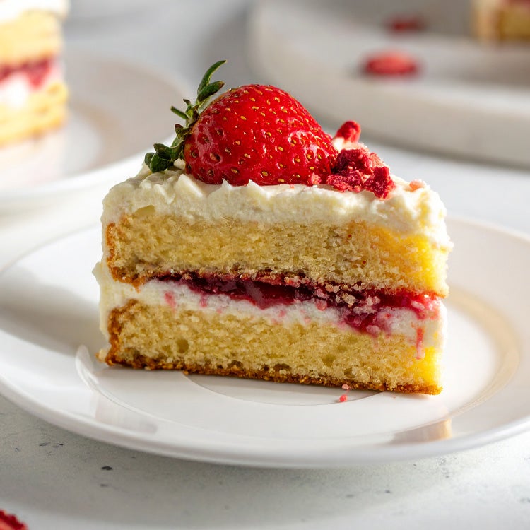 Slice of vanilla sandwich cake on a white plate, with Milkybar white chocolate buttercream and jam in the middle