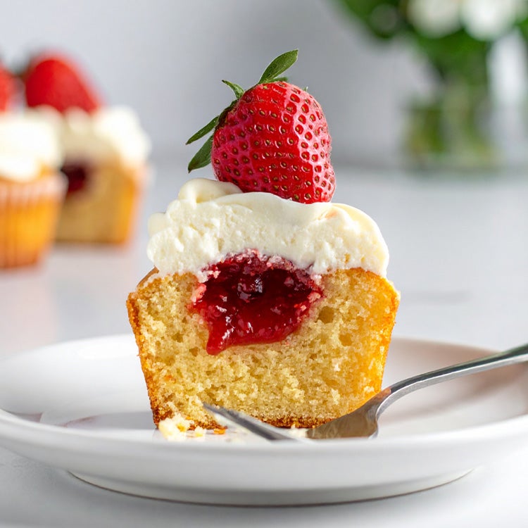 olden vanilla cupcake on a white plate, topped with Milkybar white chocolate buttercream and a fresh strawberry over a pocket