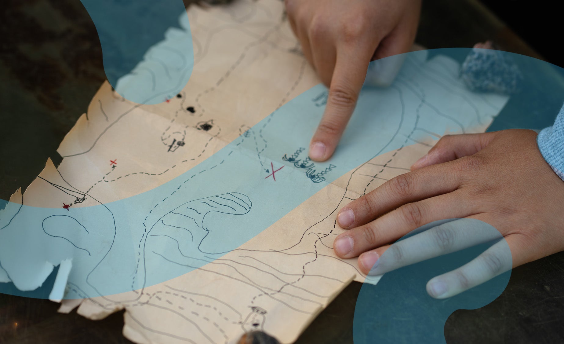 A hand-drawn map with a child’s hand pointing to the treasure