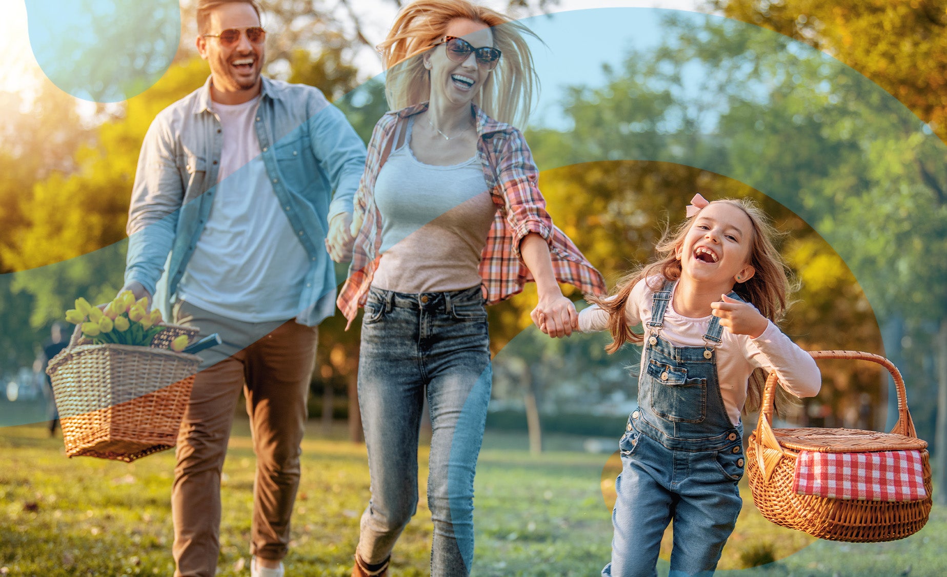  A man holding a picnic basket, laughing as his daughter pulls both him and his wife by the hand in a grass parkland 