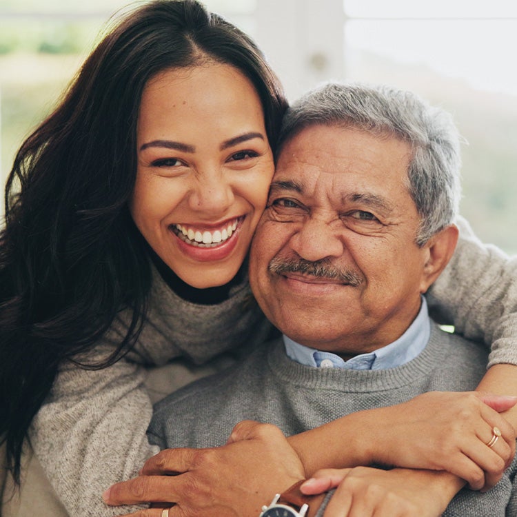 A woman hugs her elderly father on a sofa in a cosy living room 