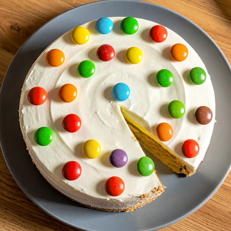 Picture of a vanilla birthday cake decorated with pale buttercream and a ring of colourful Smarties around the edge 