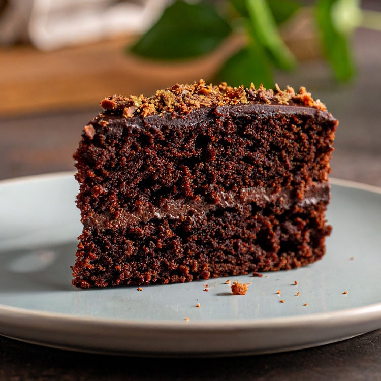 Slice of dark chocolate cake topped with crumbled Aero Orange, on a white plate 