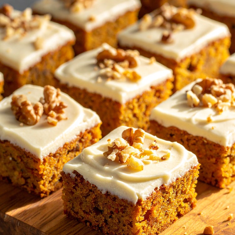 Squares of carrot cake traybake topped with Milkybar white chocolate buttercream and a sprinkling of chopped walnuts