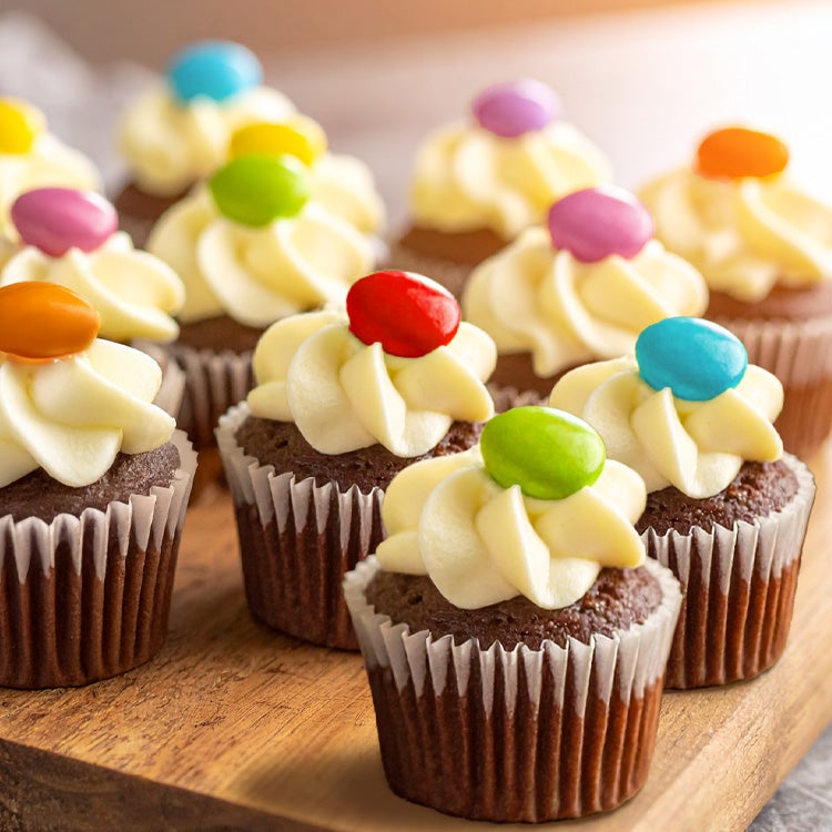 Batch of chocolate mini cupcakes on a wooden board, topped with a whirl of vanilla buttercream and one colourful Smarties
