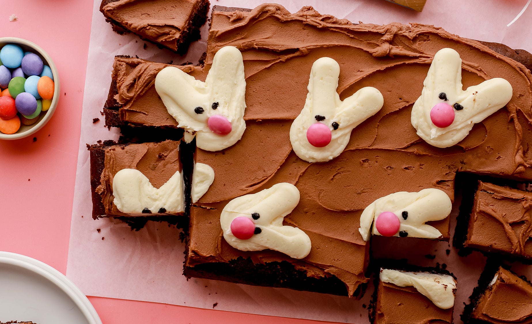 Rectangular chocolate buttercream topped cake with buttercream bunnies, with pink candy noses and small black eyes.