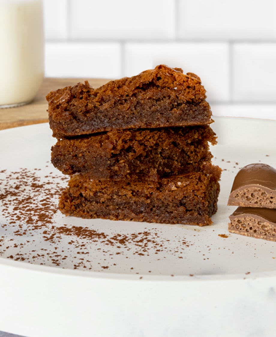 Chocolate brownies on a white plate with Aero bar stacked next to it