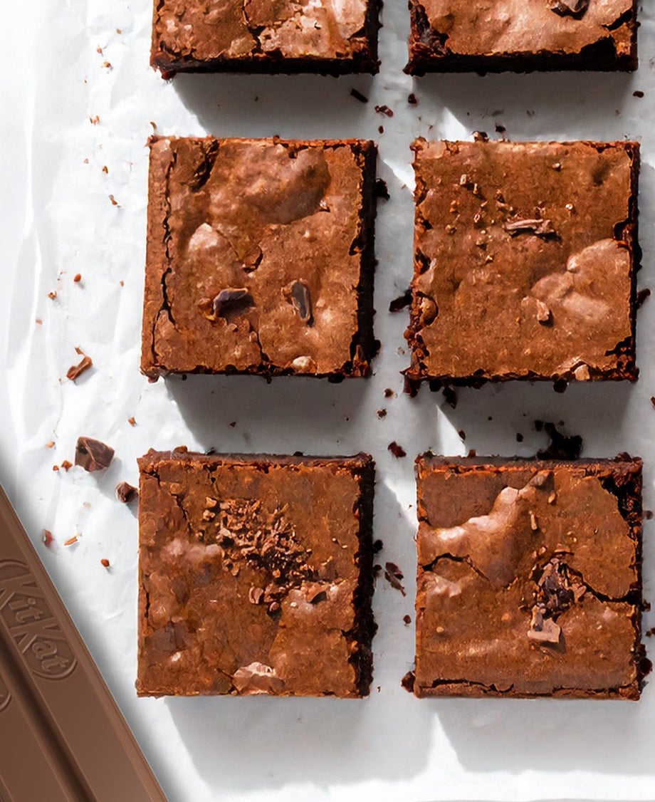 Squares of chocolate brownies made with non-visible KitKat on a piece of white baking paper, with KitKat fingers on the side