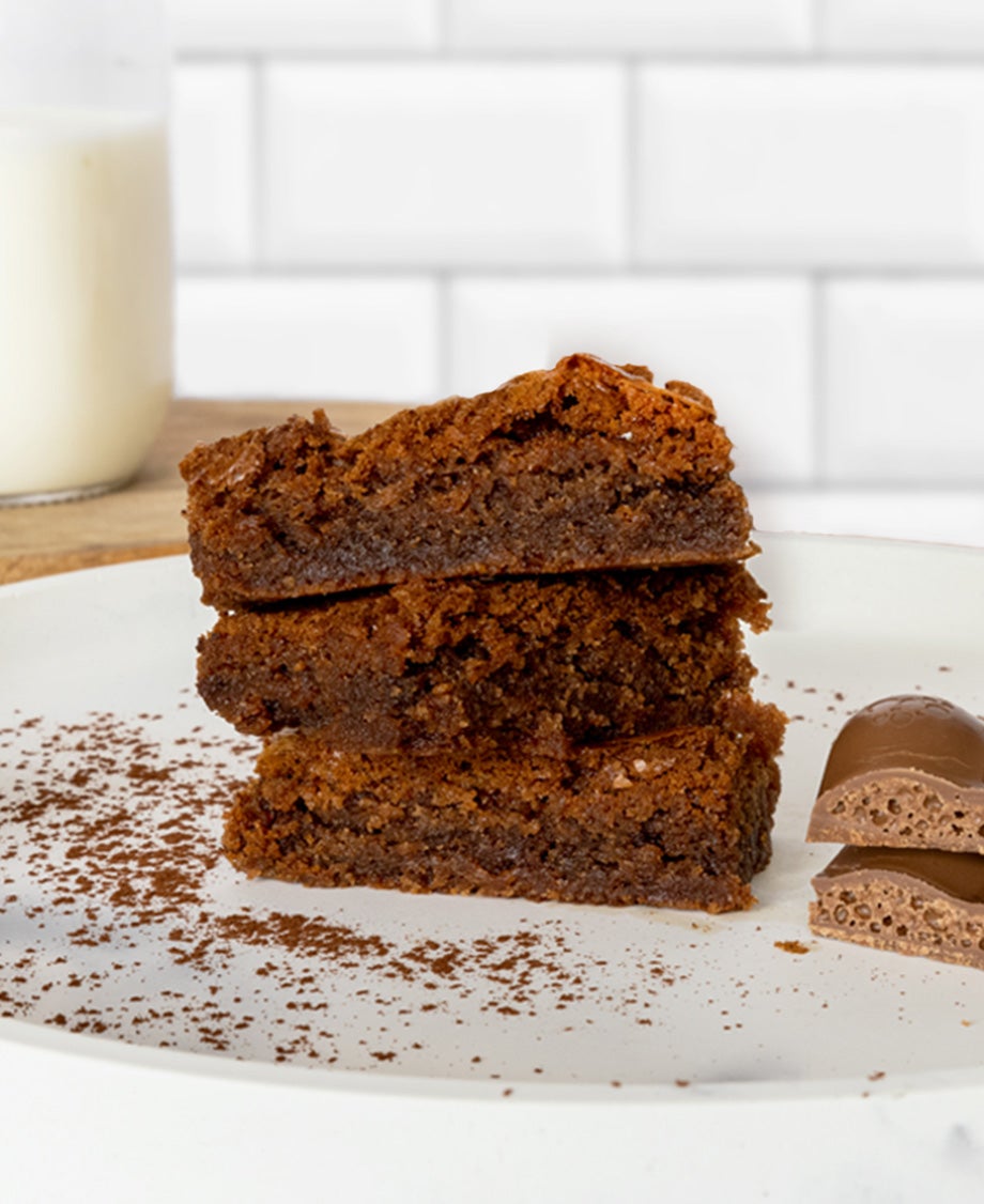 Chocolate brownies stacked up on a white plate with Aero bar placed next to it
