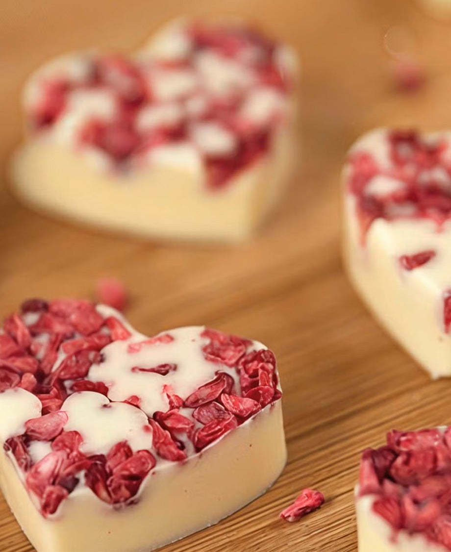 Milkybar white chocolate hearts topped with freeze-dried raspberries on a wooden board