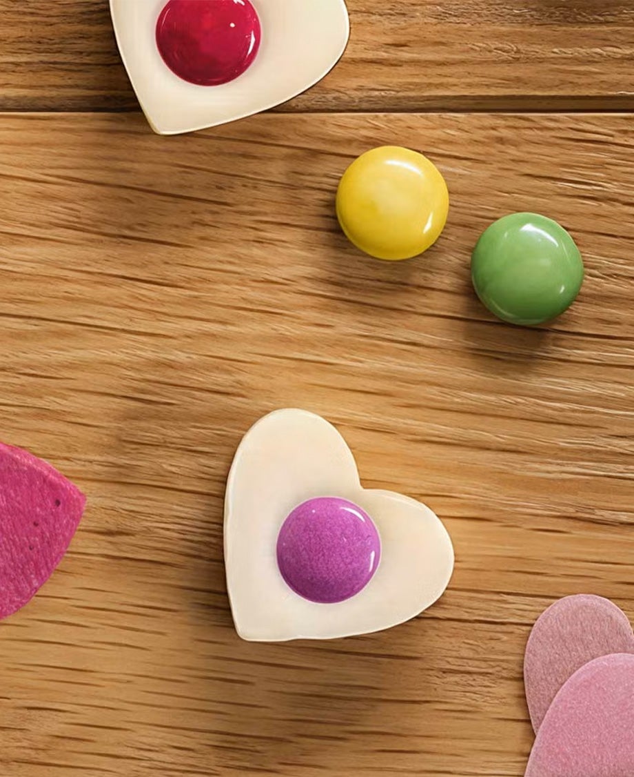 Heart-shaped Milkybar White chocolates decorated with a Smarties on a wooden surface. 